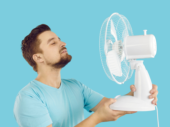 Homem com calor usando ventilador elétrico.