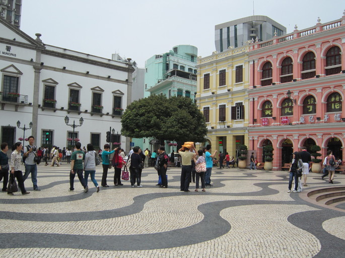 Praça em Macau cercada de prédios com arquitetura colonial portuguesa. O passeio é revestido em calçada portuguesa.