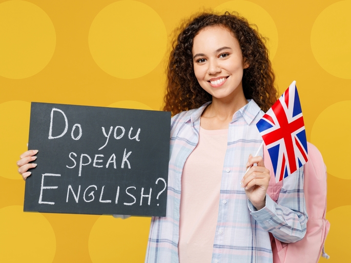 Jovem mulher segurando uma placa com a frase Do you speak english? e uma bandeira do Reino Unido